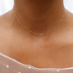 May include: A delicate gold chain necklace on a person's neck. The chain is thin and has a simple design.