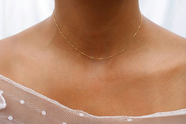 May include: A delicate gold chain necklace on a person's neck. The chain is thin and has a simple design.