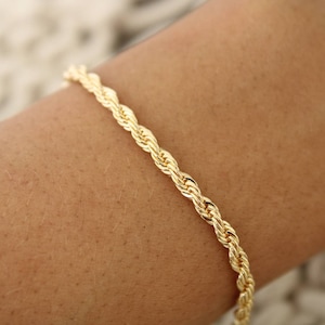 May include: A gold rope chain bracelet. The bracelet is made of a thick, twisted chain.
