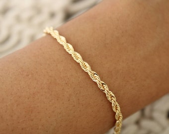 Pode incluir: Um bracelete de corrente de corda dourada. O bracelete é feito de uma corrente grossa e torcida.