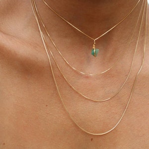 May include: A layered gold chain necklace with a small green gemstone pendant.