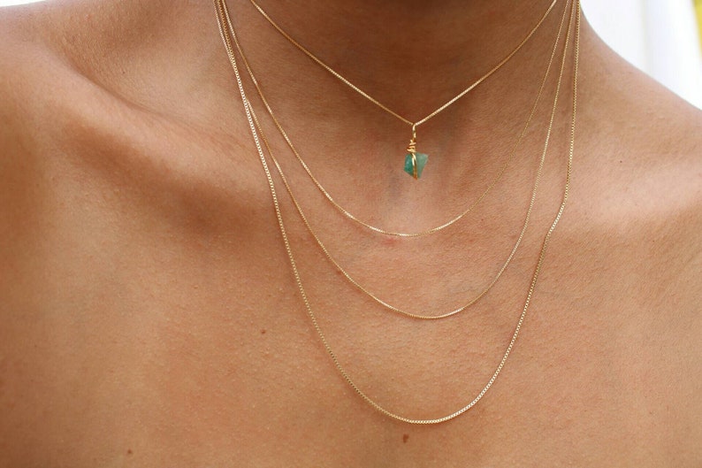 May include: A layered gold chain necklace with a small green gemstone pendant.