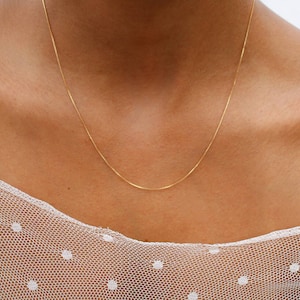 May include: A simple gold chain necklace on a person wearing a white dotted mesh top.