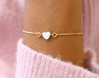 May include: A delicate gold chain bracelet with a white heart charm.
