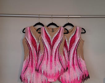 May include: Three sleeveless leotards featuring a nude-colored bodice with vibrant pink, white, and black gradient patterns. The garments are heavily embellished with sparkling silver and clear crystals arranged in intricate, symmetrical flame-like designs.