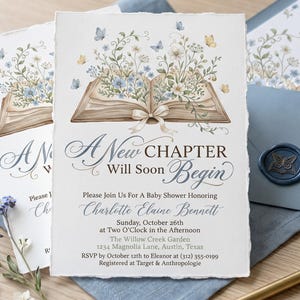 May include: A rectangular baby shower invitation with deckled edges featuring an open book illustration with wildflowers and butterflies. The text reads A New Chapter Will Soon Begin, honoring Charlotte Elaine Bennett, with event details and a blue envelope.