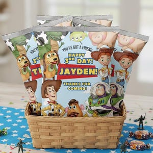 May include: A woven basket filled with several snack bags featuring characters from the Toy Story movie. The bags have the text "YOU'VE GOT A FRIEND HAPPY 3RD DAY! JAYDEN! THANKS FOR COMING!" on them. Small toy soldiers and candies are scattered around the basket.