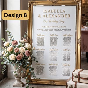 Puede incluir: Un plano de asientos de boda en un marco dorado ornamentado con fondo blanco y texto dorado que dice Isabella & Alexander Our Wedding Day. El plano enumera las mesas de la uno a la diez con nombres de invitados. Un arreglo floral est&aacute; a la izquierda.