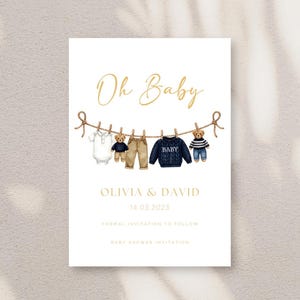 May include: Baby shower invitation with the words "Oh Baby" in gold script. The invitation features illustrations of baby clothes and teddy bears hanging on a clothesline. The names Olivia & David and the date 14.03.2023 are also included.