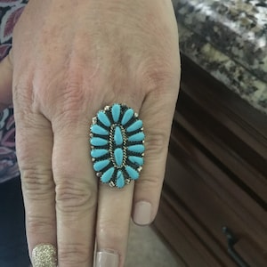Op de afbeelding: Een ring van turquoise en zilver met een cluster van turquoise stenen gezet in een zilveren band.