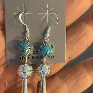 Puede incluir: Pendientes de plata con cuentas de piedra de color turquesa y un diseño floral colgante. Los pendientes se muestran en una tarjeta gris con la inscripción "STERLING SILVER". Los pendientes están en la mano de una persona.