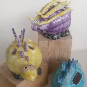 May include: Three ceramic dragon figurines, each with a different colour and design. The first dragon is purple with yellow accents, the second is yellow with purple accents, and the third is blue with white accents.