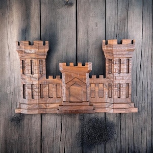 May include: A wooden carving of a castle with a brown stain finish. The castle has three towers and a central gate.