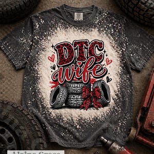 May include: A black and white t-shirt with the words "DTC wife" in red and black lettering. The shirt features a design of tires and a red bow. The shirt is handmade by Alaina Grace.