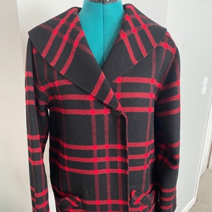 Op de afbeelding: Een zwart en rood geruite jas met een grote kraag en een enkele knoopsluiting. De jas heeft twee zakken aan de voorkant.