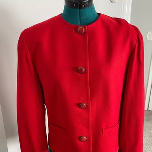 Puede incluir: Una chaqueta roja con cuatro botones rojos. La chaqueta tiene un cuello mandarín y mangas largas.