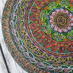 Pode incluir: Um design circular de mandala pintado em uma superf&iacute;cie de madeira. O mandala apresenta uma variedade de cores, incluindo vermelho, laranja, amarelo, verde, azul, roxo e preto. O design &eacute; intrincado e detalhado, com uma variedade de formas geom&eacute;tricas e padr&otilde;es.