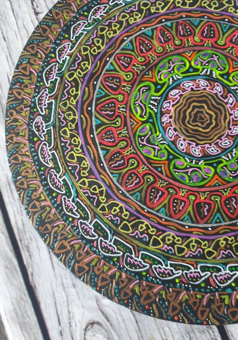 Pode incluir: Um design circular de mandala pintado em uma superf&iacute;cie de madeira. O mandala apresenta uma variedade de cores, incluindo vermelho, laranja, amarelo, verde, azul, roxo e preto. O design &eacute; intrincado e detalhado, com uma variedade de formas geom&eacute;tricas e padr&otilde;es.