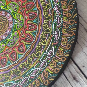Pode incluir: Uma tela circular de madeira com um design de mandala colorido pintado sobre ela. O mandala apresenta uma variedade de formas geom&eacute;tricas e padr&otilde;es em tons de rosa, amarelo, verde, azul e laranja. O design &eacute; intrincado e detalhado, e as cores s&atilde;o vibrantes e chamativas.