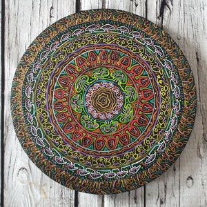 Pode incluir: Um prato redondo de madeira com um design de mandala colorido pintado nele. O mandala apresenta c&iacute;rculos conc&ecirc;ntricos de padr&otilde;es geom&eacute;tricos em tons de vermelho, verde, amarelo e azul.