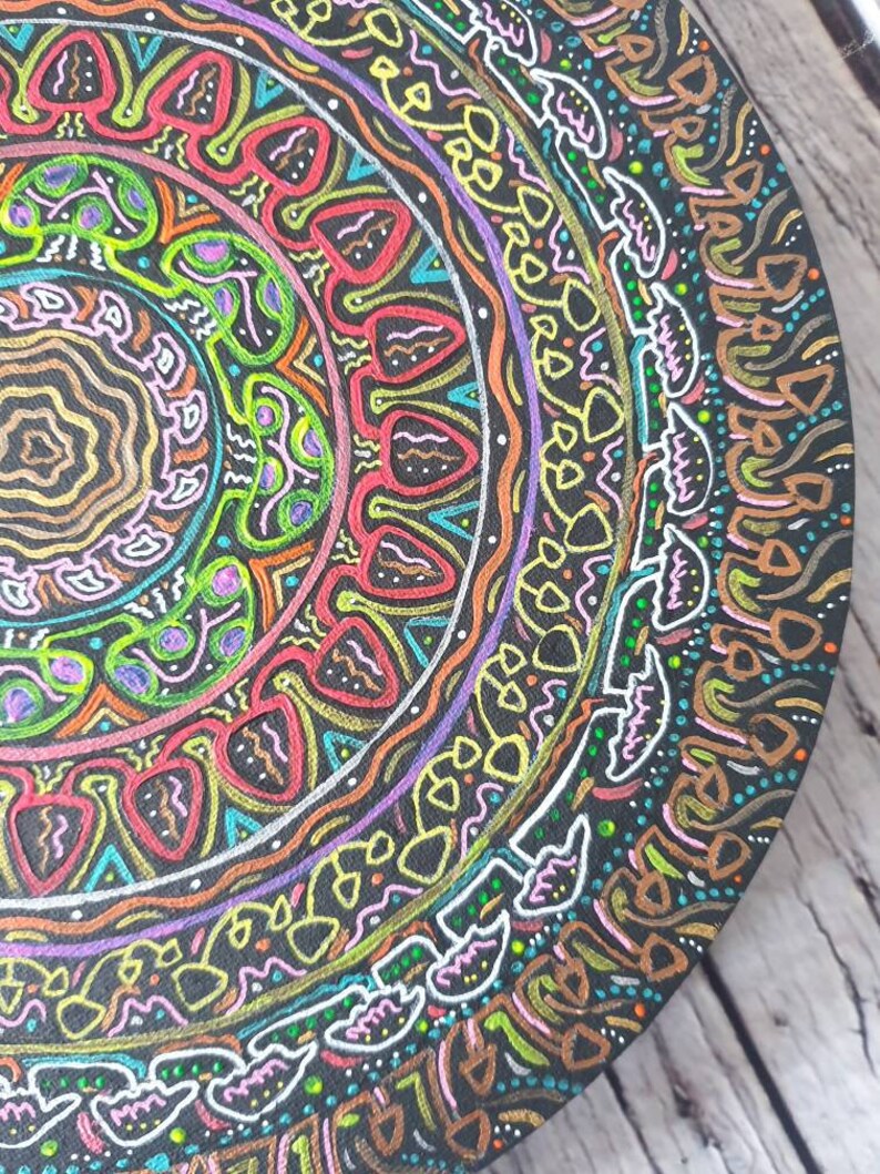 Pode incluir: Um design circular de mandala pintado em uma superf&iacute;cie preta. O mandala apresenta padr&otilde;es intrincados em tons de rosa, verde, amarelo, azul e vermelho.
