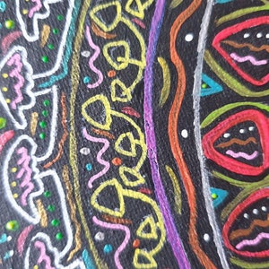 Pode incluir: Um close-up de um desenho circular de mandala pintado em uma superf&iacute;cie preta. O desenho apresenta uma variedade de cores, incluindo rosa, amarelo, verde, azul, vermelho e branco. O desenho &eacute; intrincado e detalhado, com uma variedade de formas e padr&otilde;es.