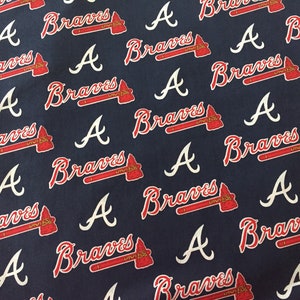 May include: Navy blue fabric with a repeating pattern of the Atlanta Braves logo. The logo includes the word "Braves" in red script and a red tomahawk, along with a white "A" symbol.