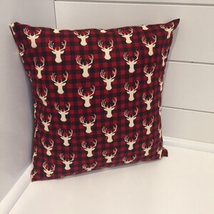 May include: Red and black plaid throw pillow with a white deer silhouette pattern.