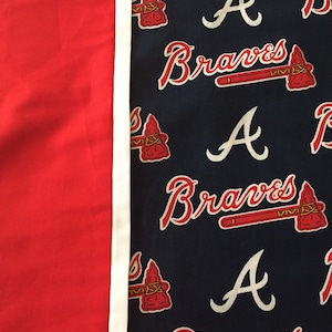 May include: A red and navy blue fabric with a white border. The navy blue side features the word "Braves" in red script, along with a red tomahawk and the letter "A".