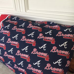 May include: A navy blue pillowcase featuring a repeating pattern of the Atlanta Braves logo and wordmark in red and white. The pillowcase has a red border.