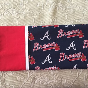 May include: A pillowcase featuring the Atlanta Braves logo and team name. The design includes the letter "A" and the word "Braves" in white script, along with a tomahawk logo, set against a navy blue background. The pillowcase has a red border.