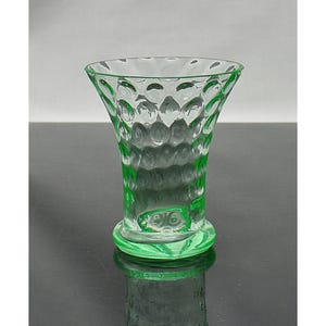Puede incluir: Un jarrón de vidrio transparente verde con una parte superior acampanada y una base circular. El jarrón tiene un patrón texturizado en forma de burbujas en el exterior. El jarrón mide aproximadamente 13 cm de alto.