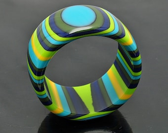 May include: A colorful striped ring with a blue, green, yellow, and black pattern. The ring is made of resin and has a glossy finish.