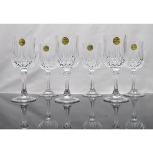 May include: Set of six clear crystal wine glasses with a diamond pattern. Each glass has a gold label that reads "Cristal D'arques".