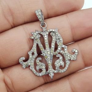 May include: A silver pendant with a delicate, ornate design featuring the letters "M" and "A" set with small, sparkling diamonds. The pendant is made of sterling silver and is perfect for adding a touch of elegance to any outfit.