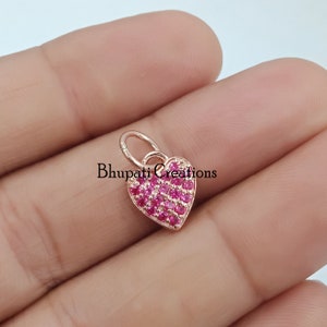 May include: A rose gold heart-shaped charm with a pink crystal design. The charm has a loop at the top for attaching to a necklace or bracelet.