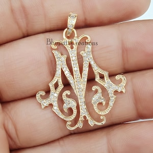 May include: A gold-colored pendant with the intertwined letters "N" and "M" encrusted with small, sparkling stones. The pendant has an ornate, filigree design and the text "Bhupati Creations" is visible.