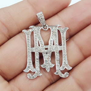 May include: A silver pendant with the letters "MM" set with small diamonds. The pendant is in the shape of a monogram.