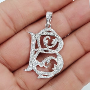 May include: Silver pendant with a large, ornate letter B made of clear cubic zirconia stones. The pendant is set against a white background.