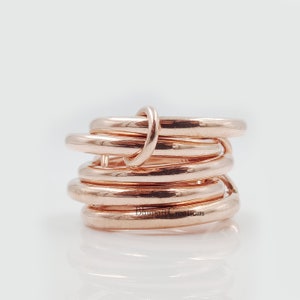 May include: A rose gold ring made of multiple intertwined bands. The ring is thick and has a polished finish.