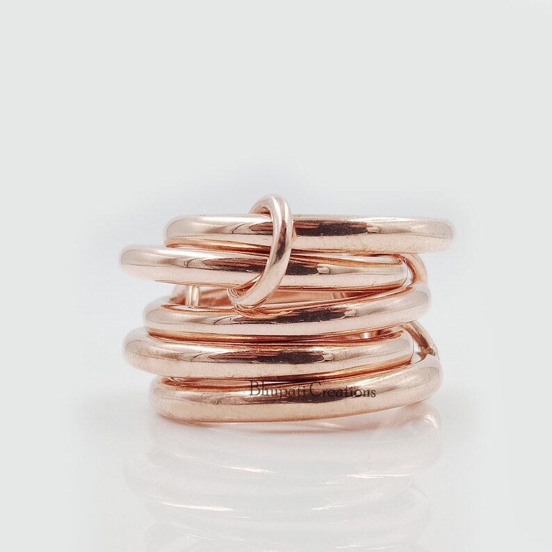 May include: A rose gold ring made of multiple intertwined bands. The ring is thick and has a polished finish.