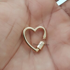 May include: Gold heart-shaped clasp with a spring-loaded closure. The clasp is made of metal and has a polished finish.