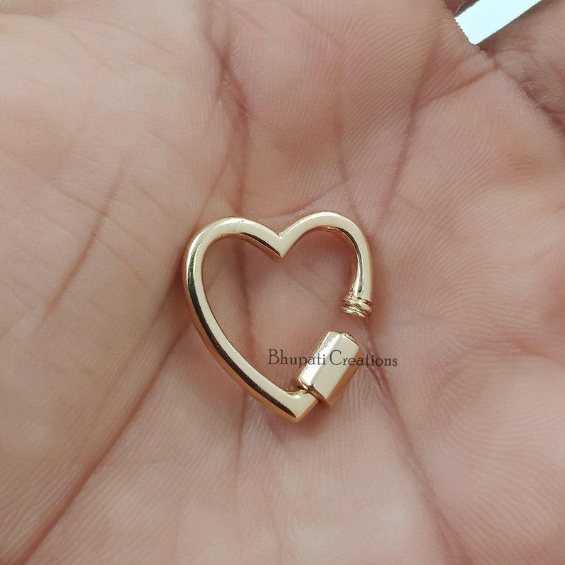 May include: Gold heart-shaped clasp with a spring-loaded closure. The clasp is made of metal and has a polished finish.