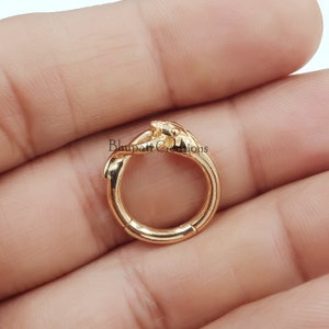 Può includere: Orecchino a cerchio clicker con cerniera dorata con un designo decorativo di due mani intrecciate.