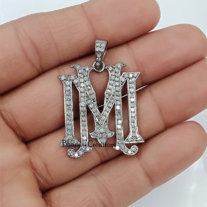 Peut inclure: Un pendentif en argent avec une initiale 'M' sertie de diamants pavés. Le pendentif est sur un fond blanc.