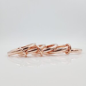 May include: Four rose gold interlocking rings. The rings are stacked on top of each other and are made of a smooth, polished metal.