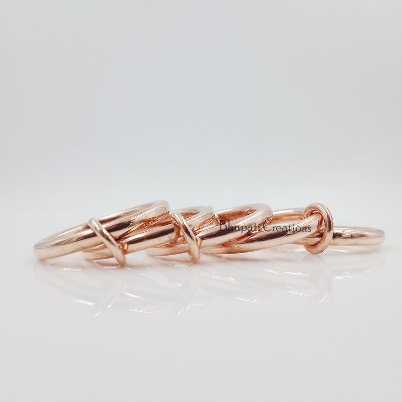 May include: Four rose gold interlocking rings. The rings are stacked on top of each other and are made of a smooth, polished metal.
