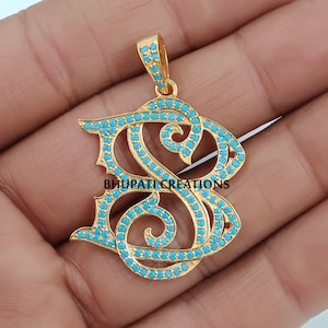 May include: Gold pendant with a turquoise blue letter 'S' design. The letter is made of gold and is set with turquoise blue stones. The pendant is on a white background.