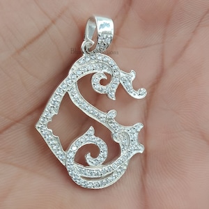 Peut inclure: Pendentif en argent avec une lettre 'S' stylisée, un design décoratif et des pierres de zircone cubique transparentes.