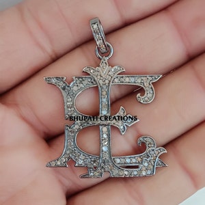 May include: A silver pendant with the letter 'E' in a decorative script style, encrusted with small diamonds. The pendant is on a silver chain.
